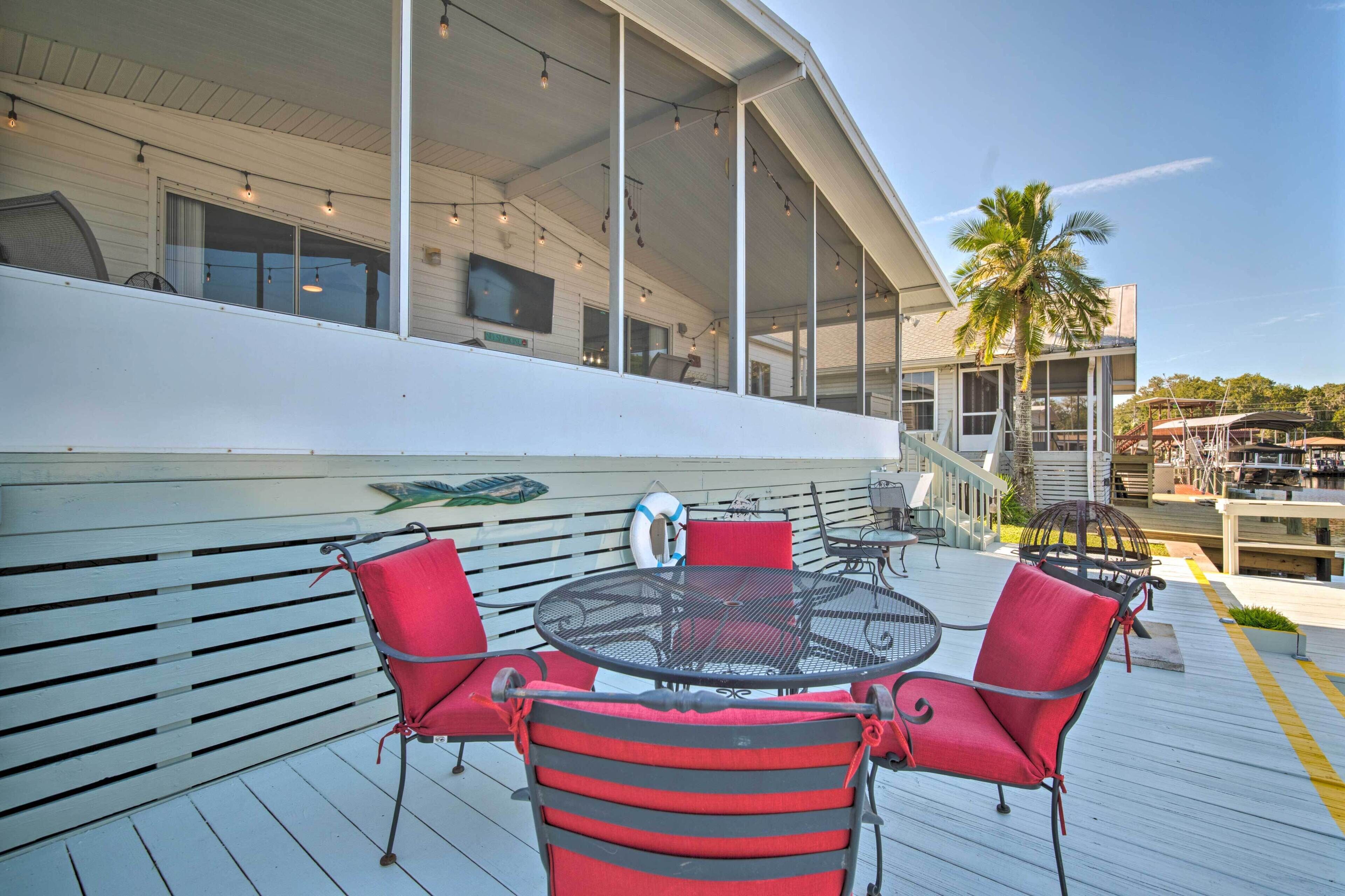 A covered outdoor seating area with a round table and four red chairs, a lifebuoy, and a palm tree in the background.