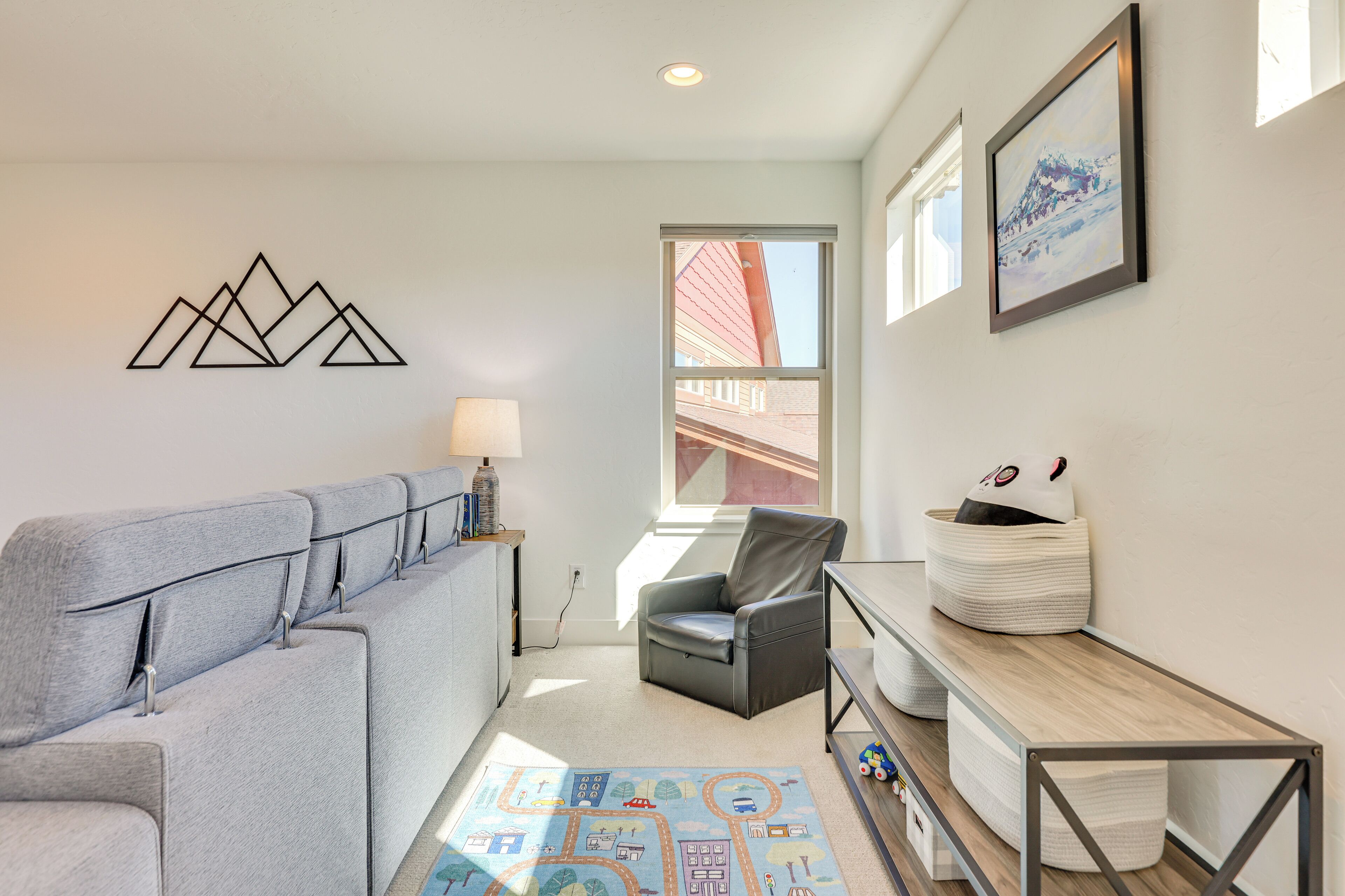 Een moderne woonkamer met een grijze bank, een zwarte lederen fauteuil, een houten salontafel en een kleurrijk vloerkleed.