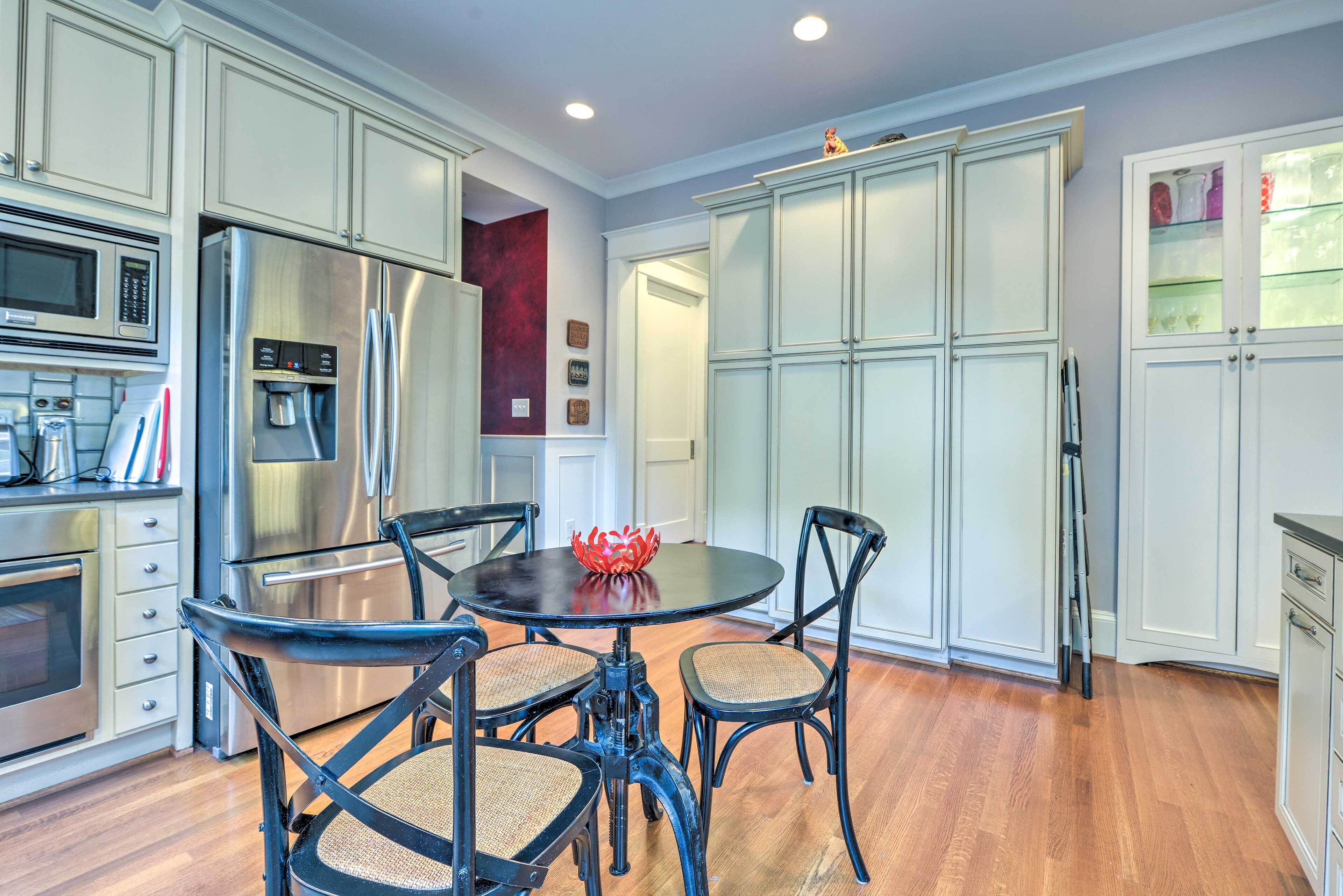 A modern kitchen with white cabinetry, stainless steel appliances, and a round dining table with black chairs.