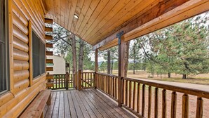 Une véranda en bois avec un banc, une balustrade et une vue sur des arbres et un bâtiment en arrière-plan.