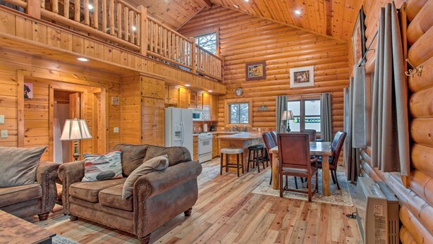L’intérieur d’une cabane en rondins comprend un coin repas, une cuisine et un salon confortable avec un canapé et des fauteuils.