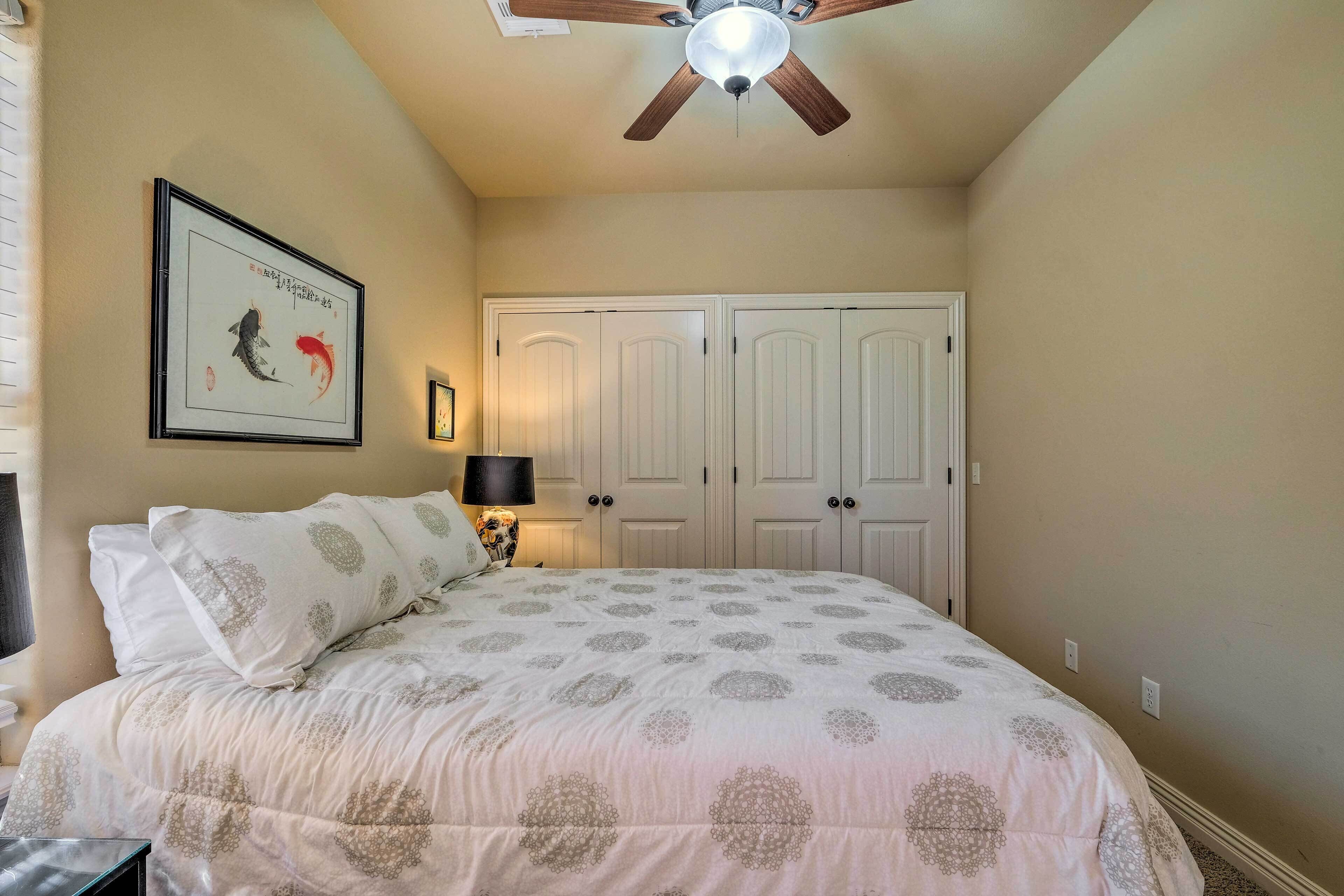 A bedroom with a bed, a ceiling fan, a framed artwork, and a set of double doors.