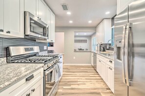 A modern kitchen with stainless steel appliances, white cabinets, and a wooden floor. - Walk to UF: Family Home w/ Patio! (Gainesville)