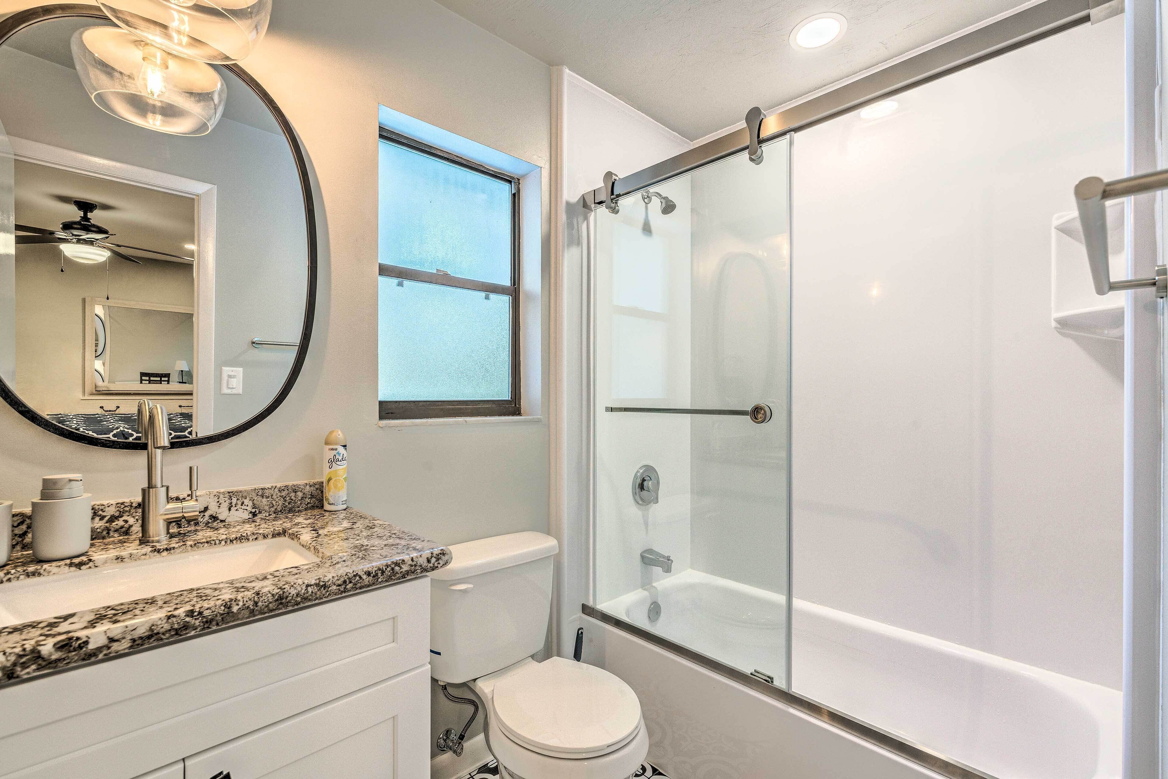 A modern bathroom with a granite countertop, a toilet, a glass-enclosed shower, and a ceiling fan.