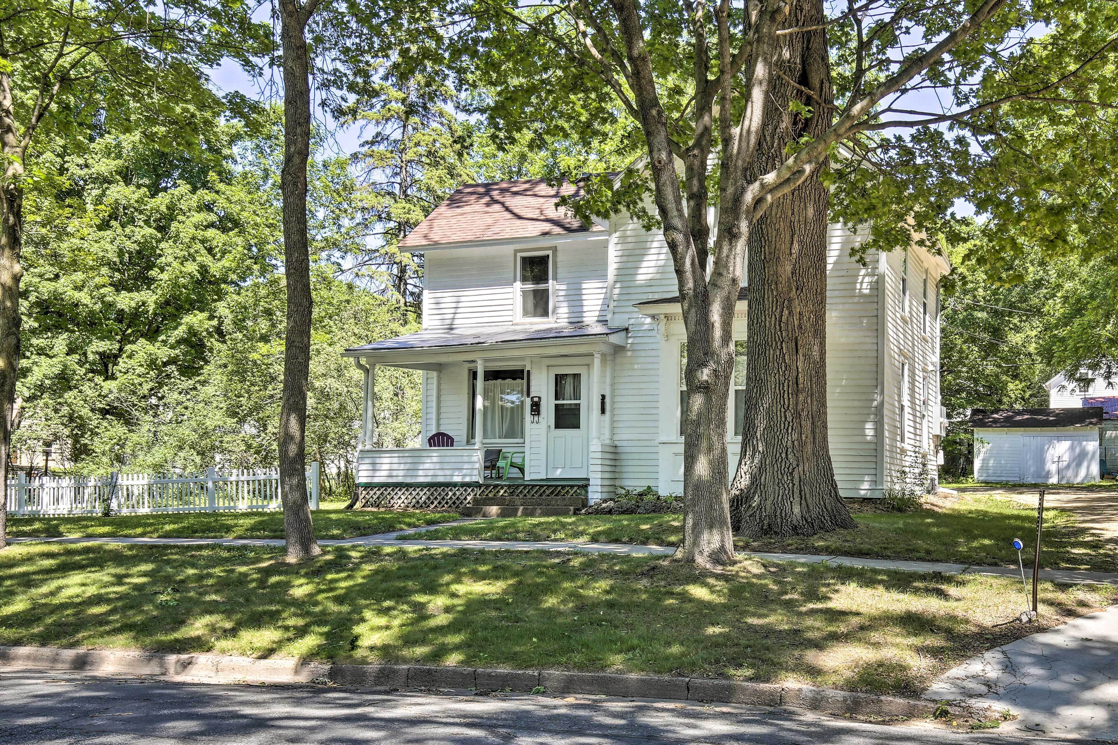 A two-story house with a porch and a large tree in front.