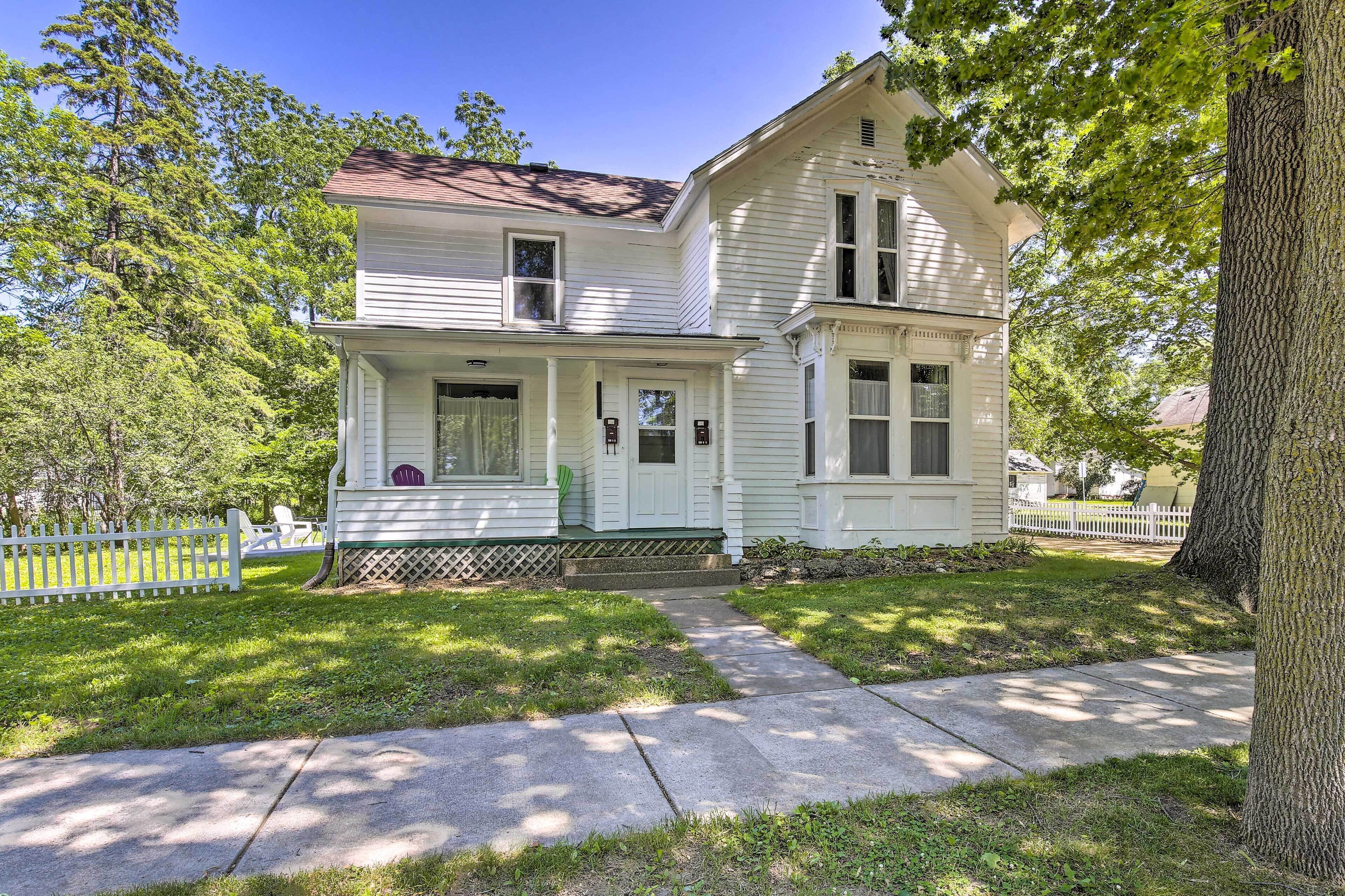 A two-story white house with a front porch, a picket fence, and a well-maintained lawn.