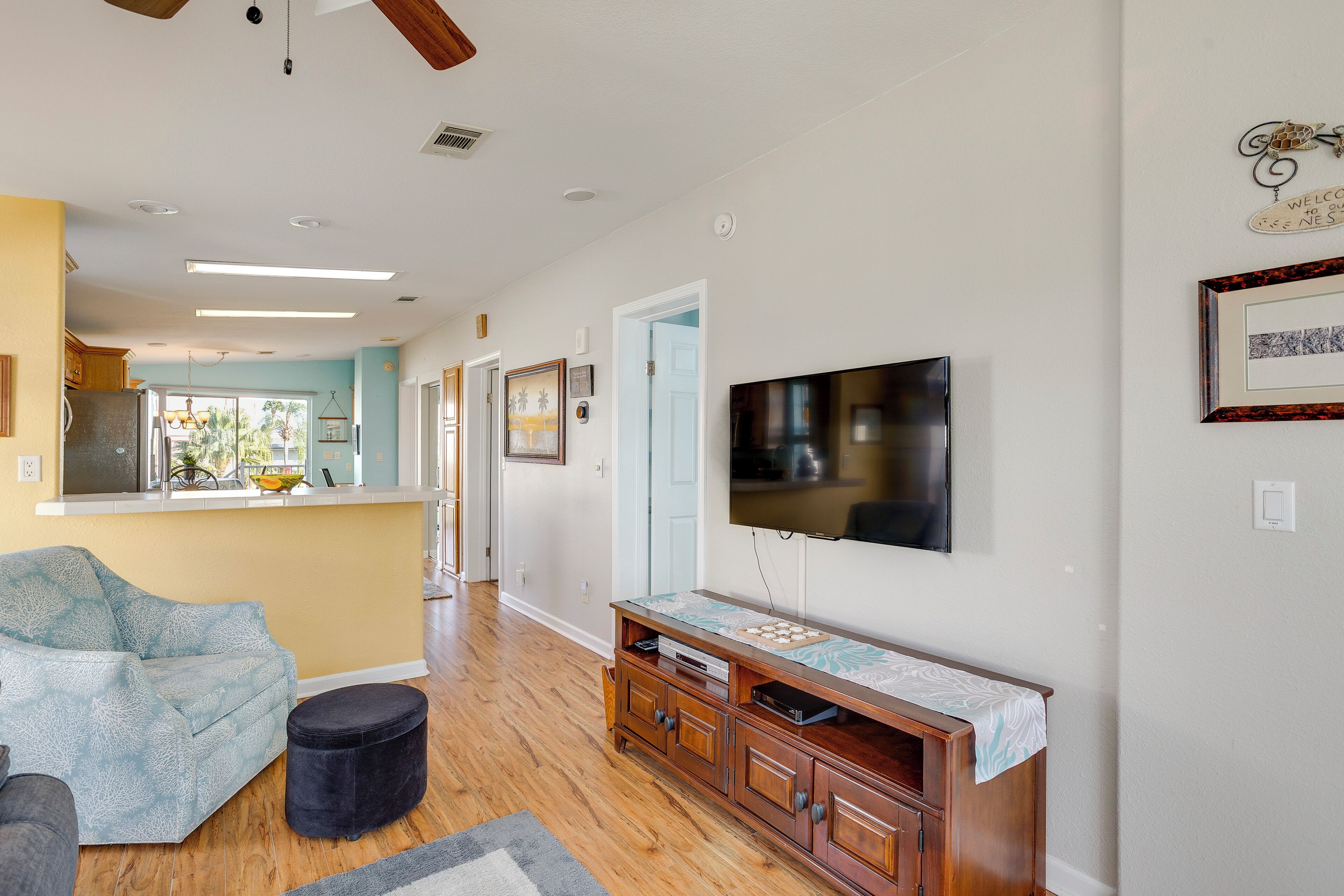 A living room with a wooden entertainment center, a flat-screen TV mounted on the wall, and a light blue patterned sofa.