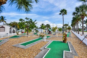 Play a round of golf amidst lush palm trees and a picturesque white picket fence.