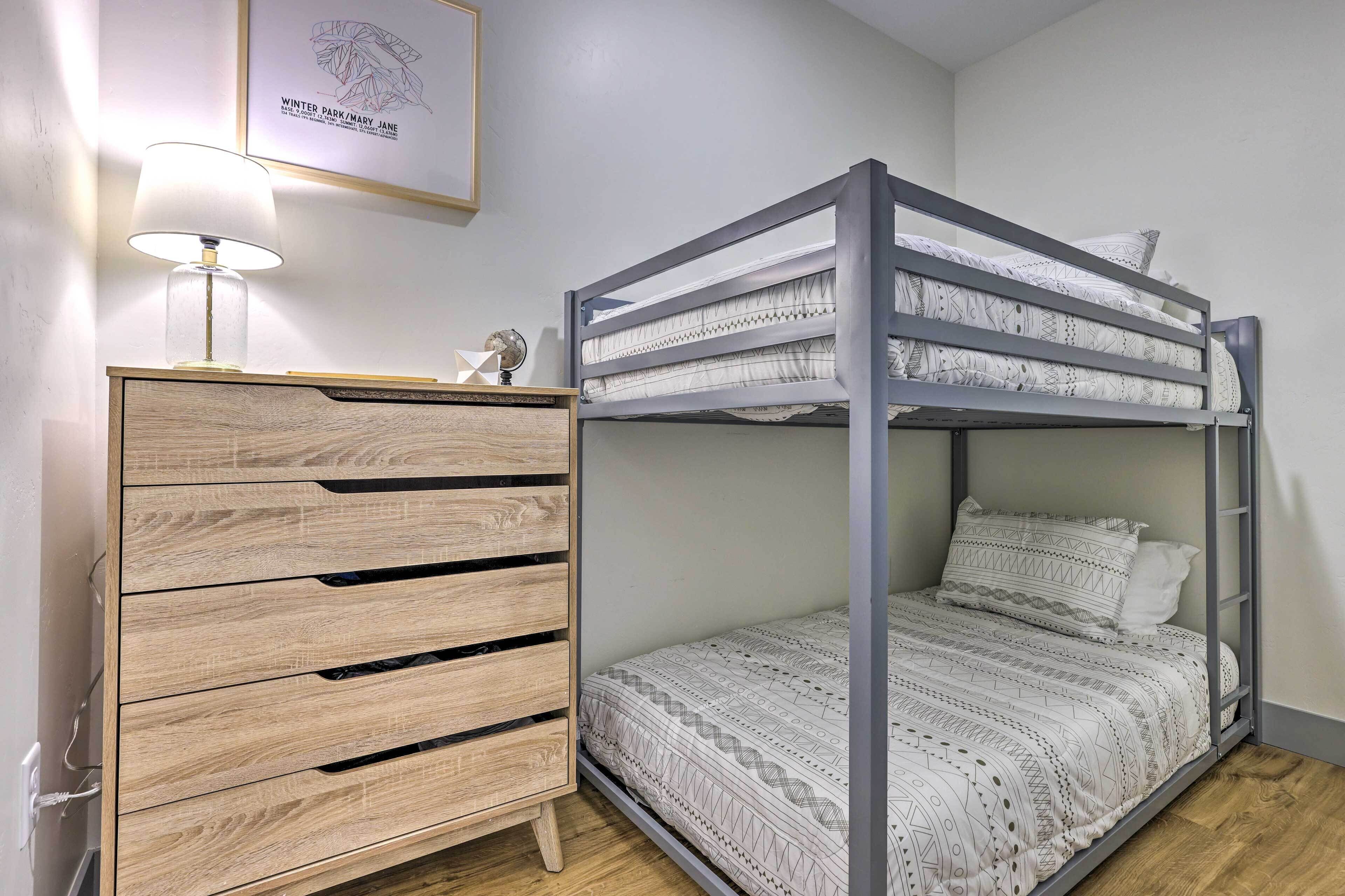 A bunk bed with patterned bedding, a wooden dresser with drawers, a globe, and a framed map on the wall.