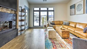 A modern living room with a large window, a leather sofa, a coffee table, and a fireplace. - Condo w/ Mountain Views in Heart of Downtown! (Winter Park)