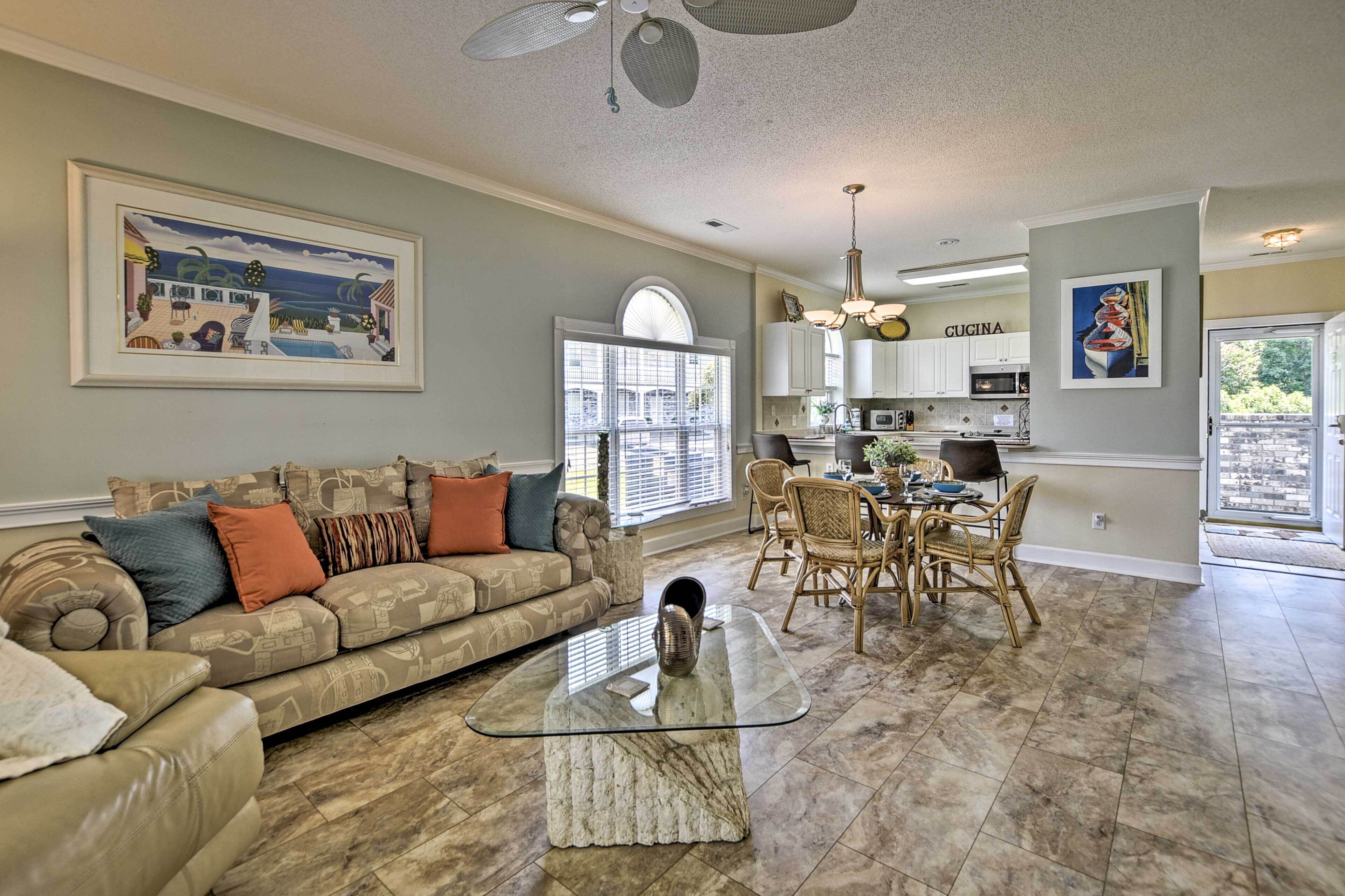 A spacious living room with a large sofa, a glass coffee table, and a dining area with wicker chairs.