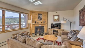 A cozy living room with a fireplace, large windows, and a TV. - Condo w/ Views & Hot Tub Access in Silverthorne! (Silverthorne)