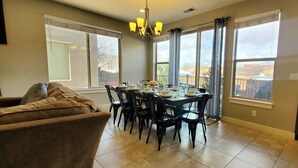 A dining area with a table set for four, a sofa, and large windows with curtains. - Entrada at Moab 652 (Moab)