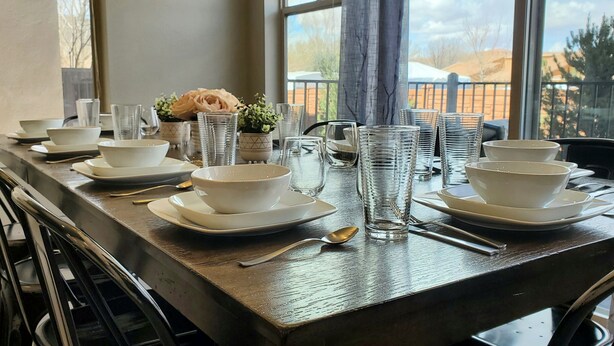 A dining table set with white bowls, plates, and clear glasses, with a view of a mountainous landscape through large windows. - Entrada at Moab 652 (Moab)