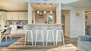 Une cuisine moderne avec des meubles blancs, un îlot central doté de tabourets de bar, un éclairage suspendu et une horloge au mur.