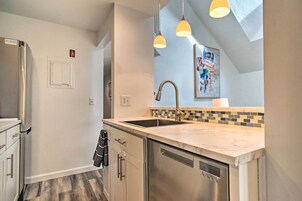 A modern kitchen with a stainless steel refrigerator, a double sink, and a dishwasher. There are pendant lights above the sink and a tiled backsplash.
