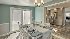 A dining area with a table set for four, a chandelier, and a kitchen in the background. - Pet-friendly Revere Getaway, Steps From the T! (Revere)