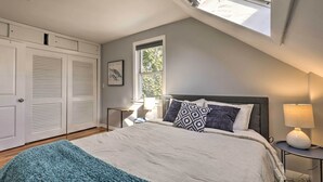 A bedroom with a skylight, a bed with patterned pillows, a bedside lamp, and a window with a view of greenery. - Pet-friendly Revere Getaway, Steps From the T! (Revere)