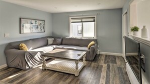 A modern living room with a grey sectional sofa, a wooden coffee table, and a large window with blinds. - Pet-friendly Revere Getaway, Steps From the T! (Revere)
