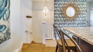 Un escalier avec une rampe en bois, un lustre et un mur orné d’un motif décoratif, agrémenté d’un miroir.