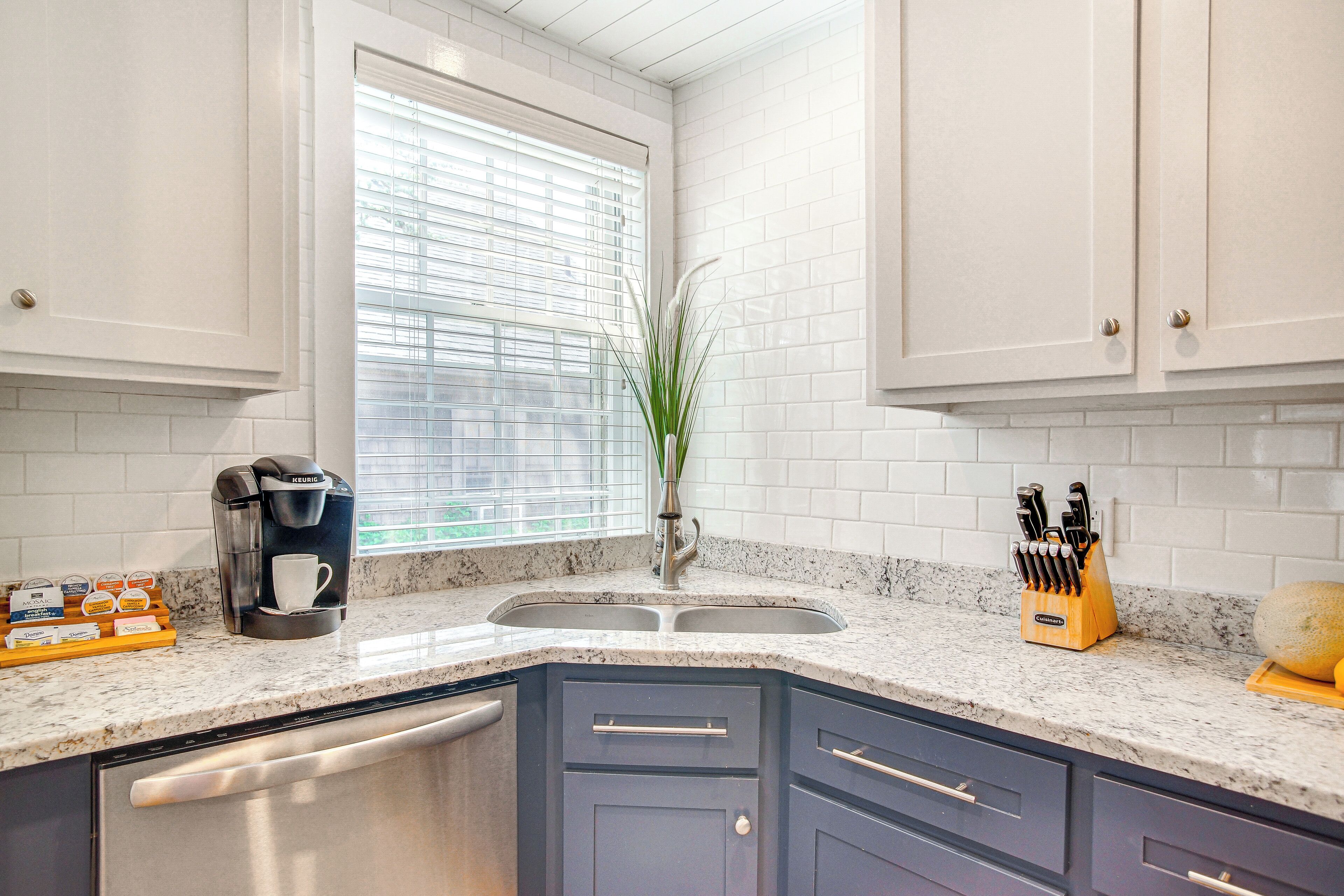 A kitchen with white tiled walls, a built-in coffee maker, a sink, and a knife block.