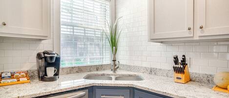 A kitchen with white tiled walls, a built-in coffee maker, a sink, and a knife block.