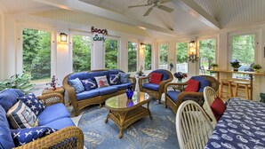 A sunroom with wicker furniture, a ceiling fan, and large windows offering a view of the greenery outside. - Mashpee House w/ Wraparound Deck - Walk to Beach! (Mashpee)