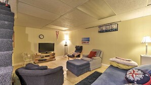 A living room with a TV, two armchairs, a sofa, a lamp, and a clock on the wall. - Mashpee House w/ Wraparound Deck - Walk to Beach! (Mashpee)