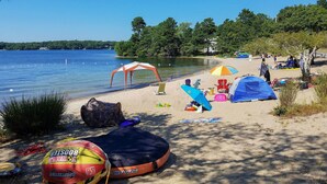 A beach with tents, beach chairs, and a lifeguard stand. - Mashpee House w/ Wraparound Deck - Walk to Beach! (Mashpee)