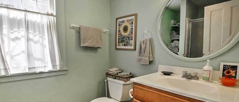 Une salle de bain avec des toilettes, un lavabo, un miroir et une fenêtre avec des rideaux.