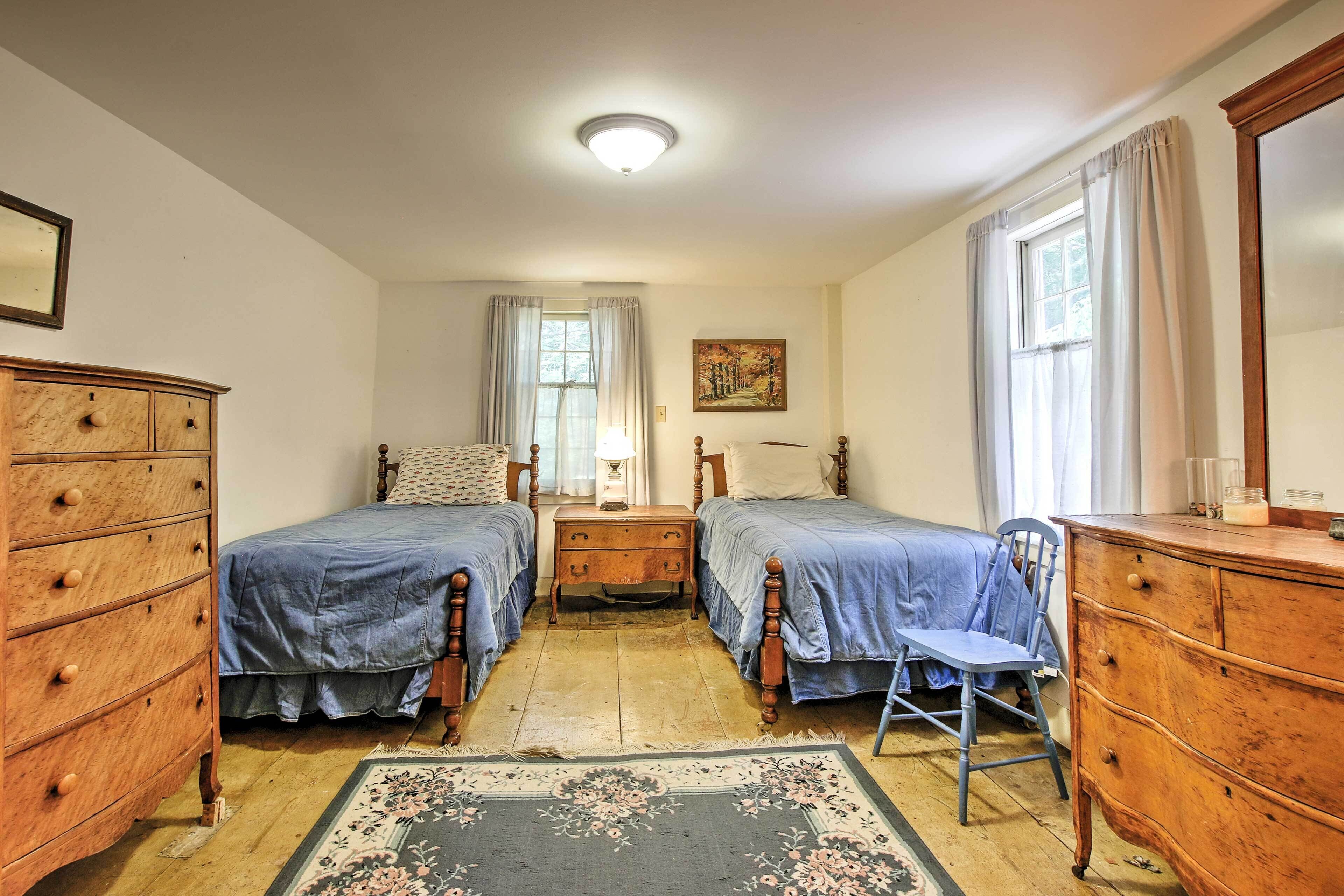 A room with two wooden beds, a wooden dresser, a chair, a nightstand with a lamp, and a painting on the wall.