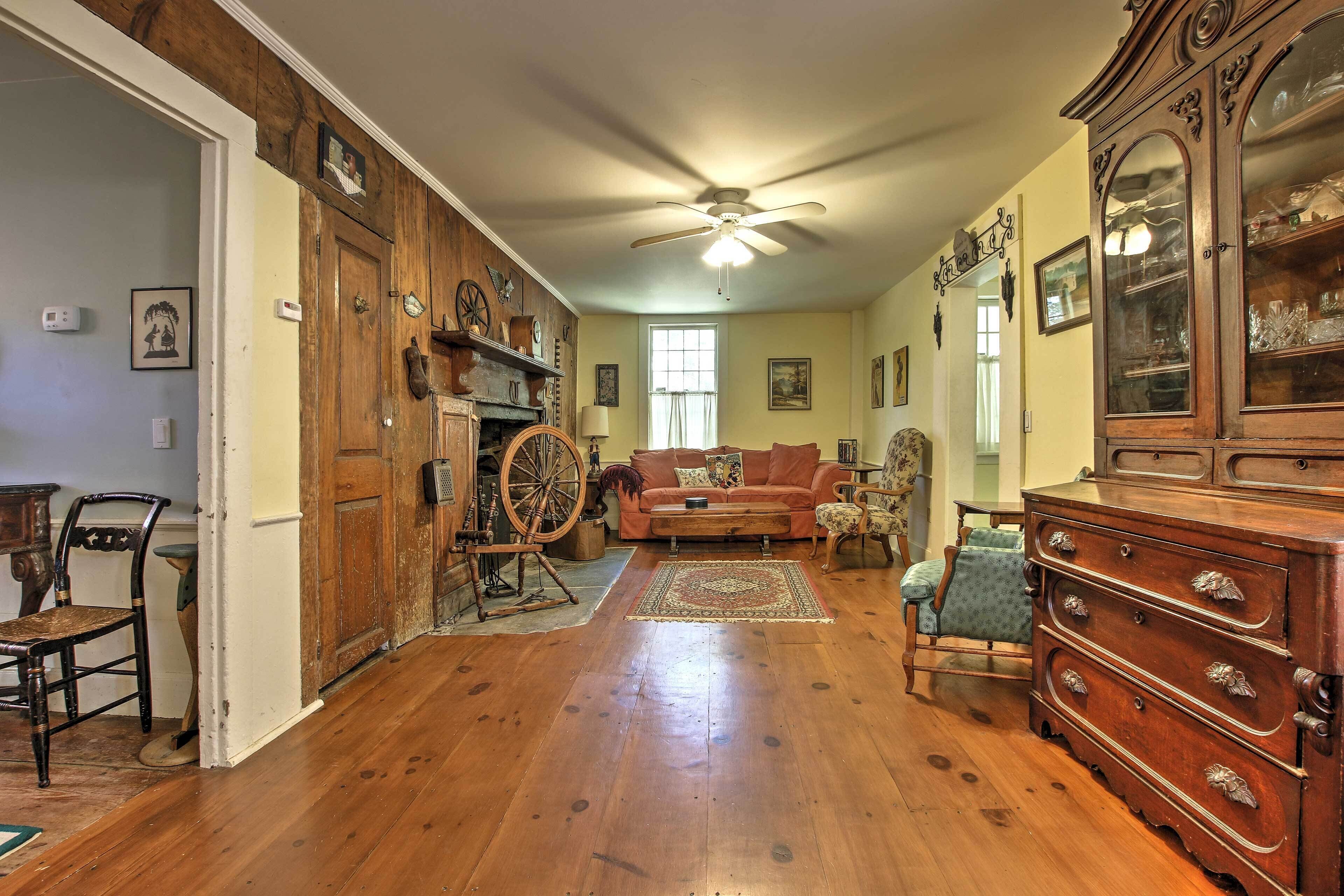A spacious room with hardwood flooring, a ceiling fan, a large wooden cabinet, and a vintage spinning wheel.