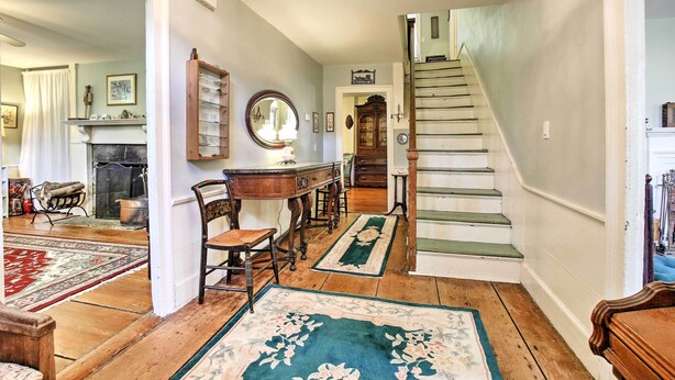 A spacious living room with a fireplace, wooden flooring, and a staircase leading to an upper level. - Historic Huntington Home - Walk to Westfield River (Huntington)