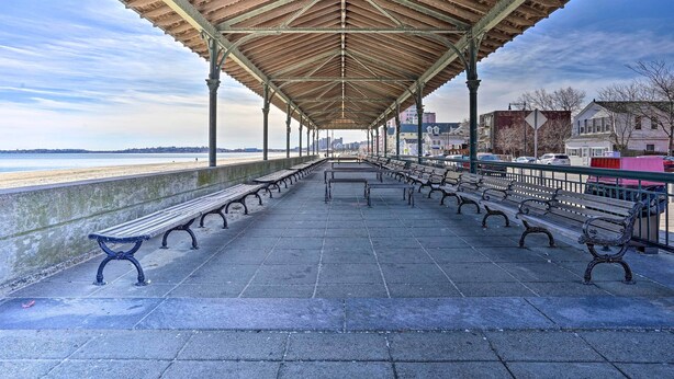 Une promenade abritée, dotée de bancs, qui offre une vue sur la plage et sur les bâtiments situés à l’arrière-plan.