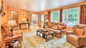 A spacious living room with leather sofas, a coffee table, and a large window with curtains. - Granby Home w/ Deck < 1/2 Mi to Aldrich Lake! (Granby)
