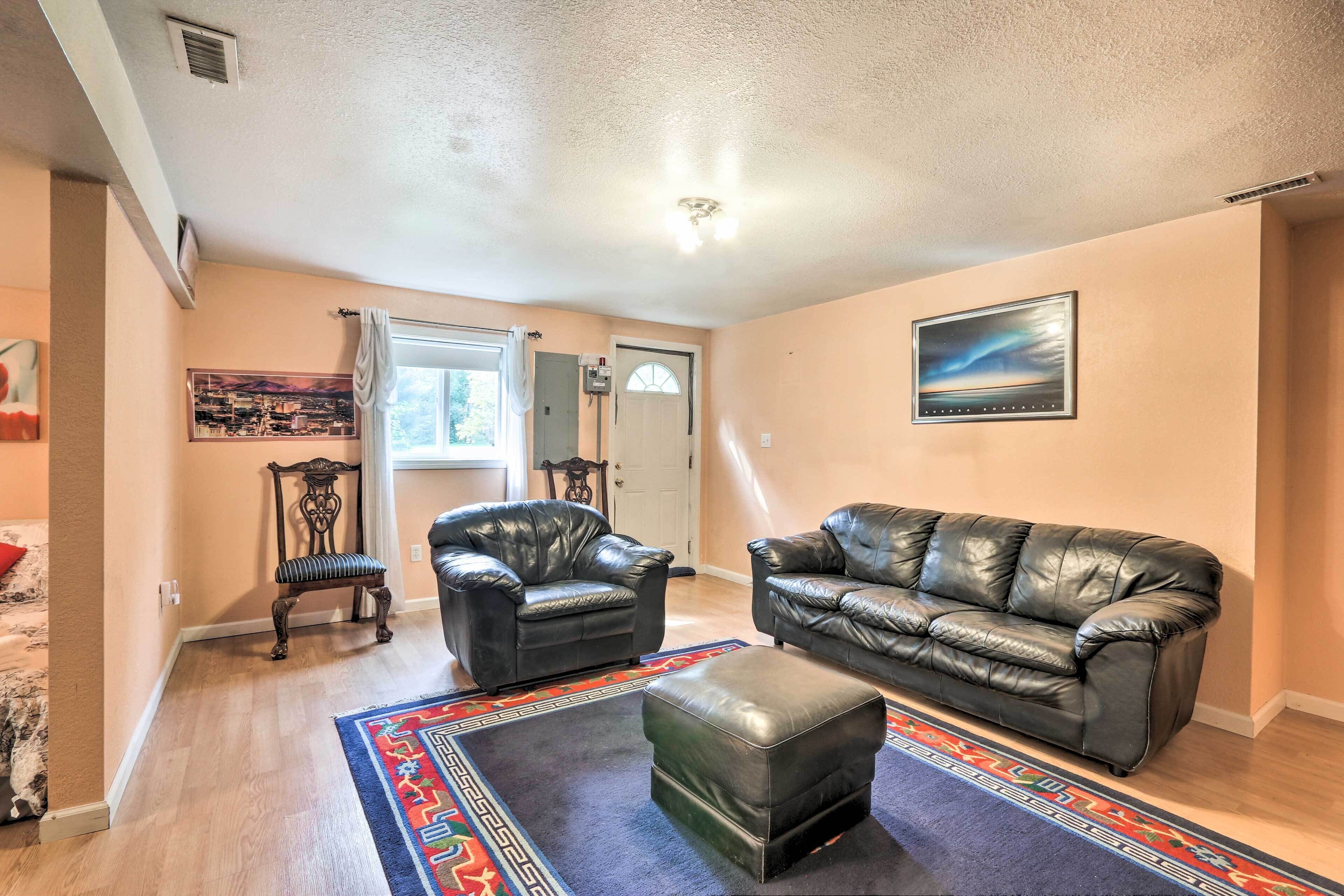 A living room with a black leather sofa, a matching ottoman, and a patterned rug.
