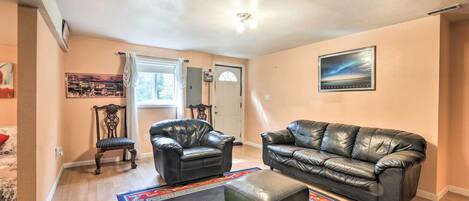 A living room with a black leather sofa, a matching ottoman, and a patterned rug.