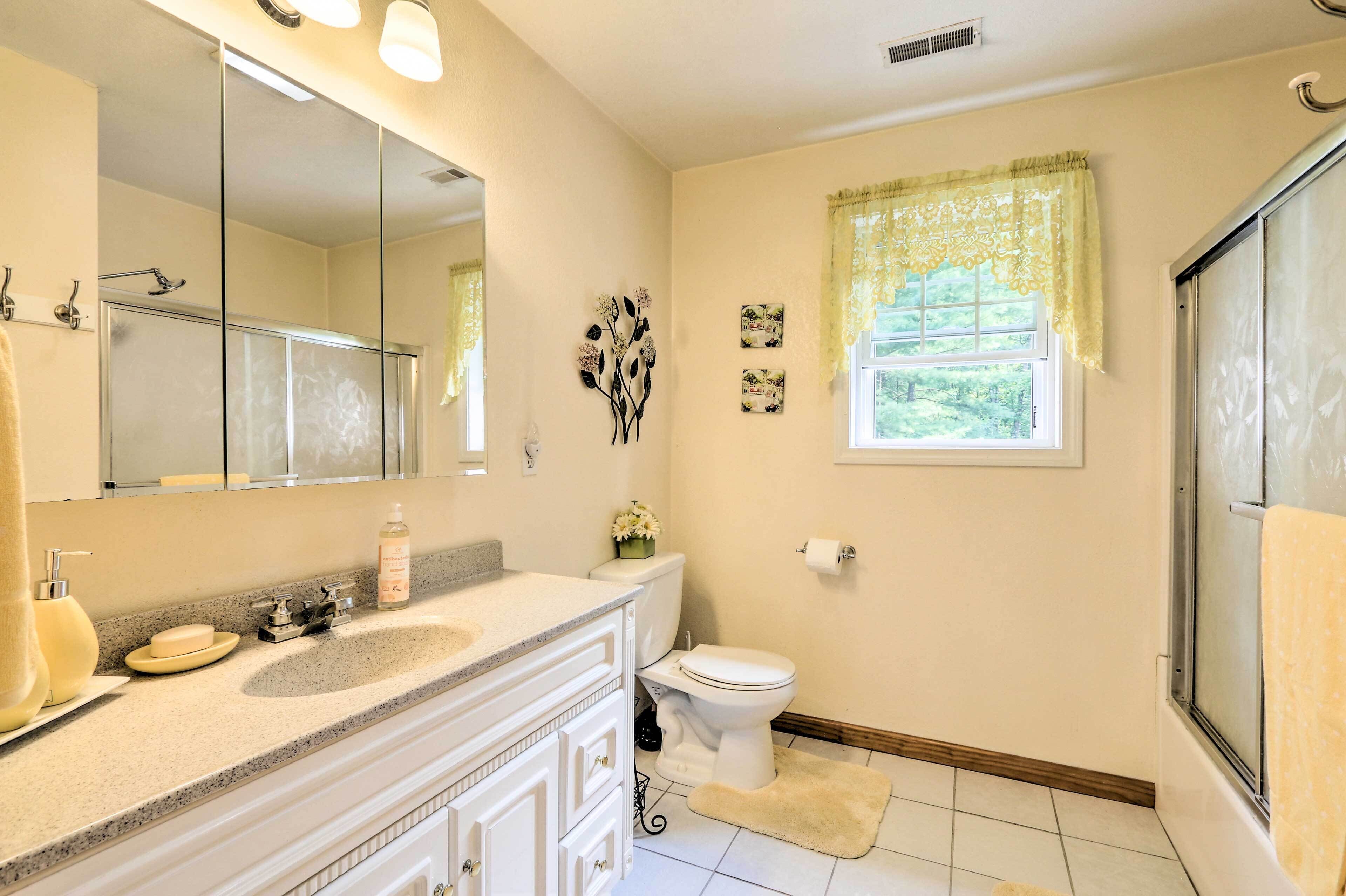 A bathroom with a sink, mirror, toilet, and window with a curtain.