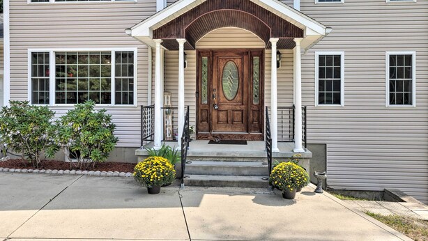 A two-story house with a front porch, a wooden door, and two potted yellow flowers. - Granby Home w/ Deck < 1/2 Mi to Aldrich Lake! (Granby)