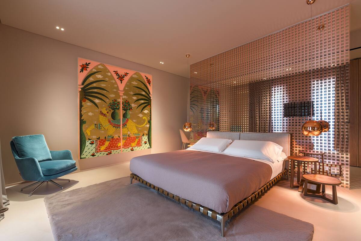 Un dormitorio moderno con una cama grande, un sillón azul y un cuadro abstracto de colores en la pared.