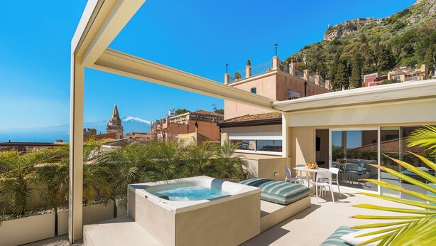 A rooftop terrace with a hot tub, seating area, and a view of a cityscape and mountains. - Taormina Infinity Suites (Taormina)