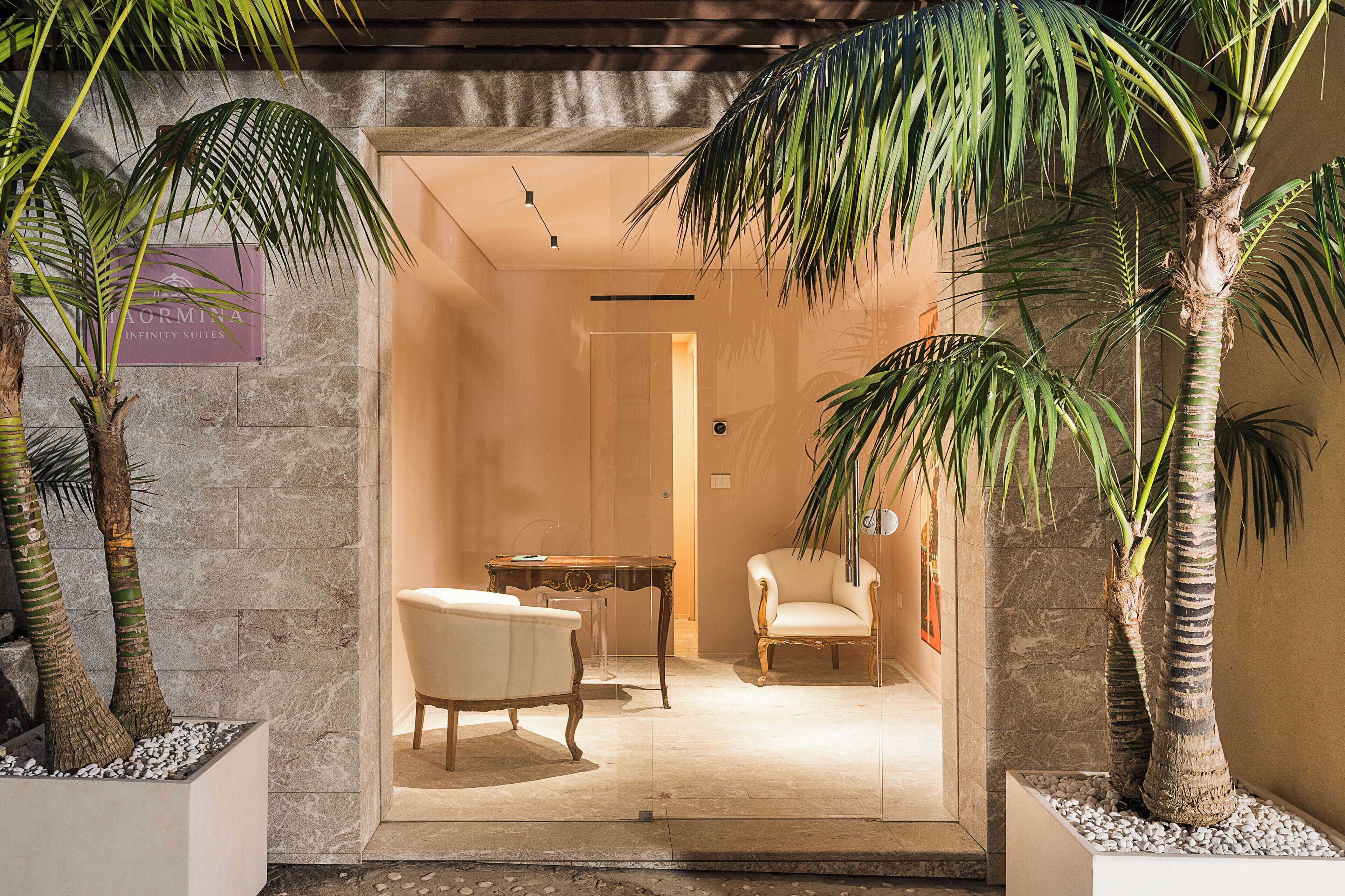 L’entrée d’un hôtel, avec un palmier, une chaise blanche et une petite table.