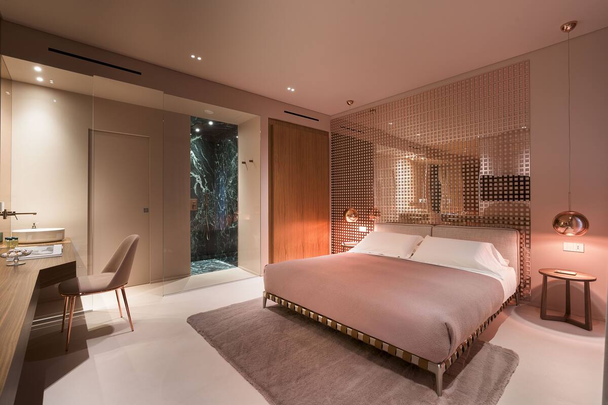 Un dormitorio moderno con una cama grande, un escritorio con silla y un baño con puerta de vidrio.