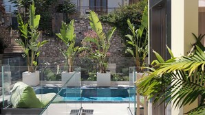 A modern outdoor pool area with glass railings, potted plants, and a stone wall in the background. - Taormina Infinity Suites (Taormina)