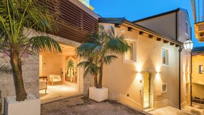 A courtyard with palm trees, a stone wall, and a building entrance with a door and windows. - Taormina Infinity Suites (Taormina)
