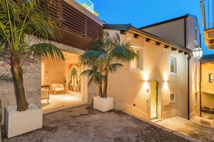 A courtyard with palm trees, a stone wall, and a building entrance with a door and windows.