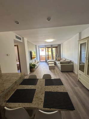 A spacious living area with a dining table, sofas, and a view through a glass door to an outdoor patio. - Oasis of Peace in Torrevieja – Luxury Residence, 3 Pools & 2 min from the Sea (Torrevieja)