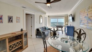 Ein Wohnzimmer mit einem Glastisch, einem Deckenventilator, einem Sofa und Blick auf den Ozean.