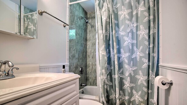 A bathroom with a white sink, a mirror, a toilet, and a shower curtain with starfish patterns. - 1 Mi to Beach: Home w/ Deck & BBQ in East Falmouth (East Falmouth)