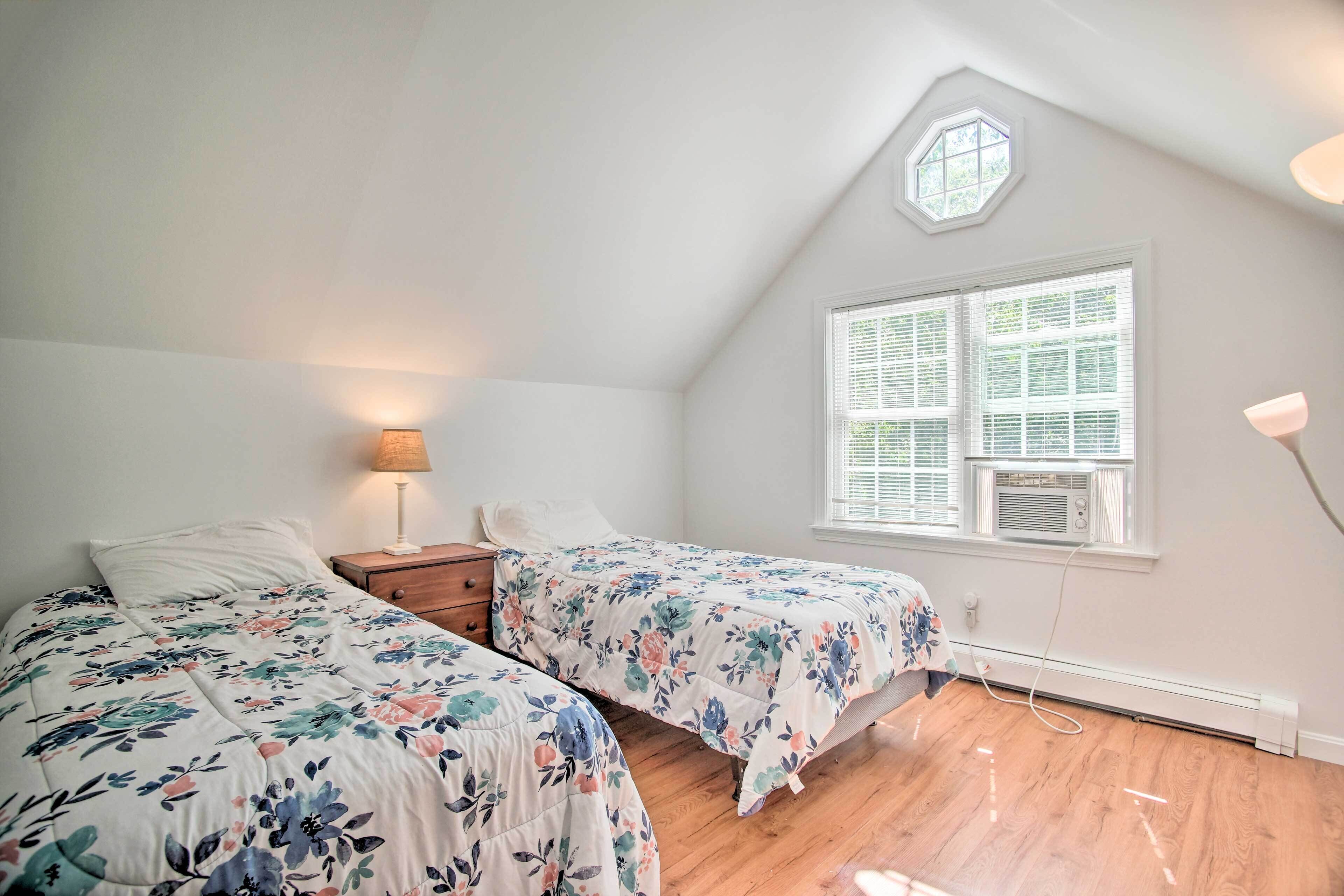 A bedroom with two beds, a nightstand, a lamp, a window with blinds, and a ceiling light.